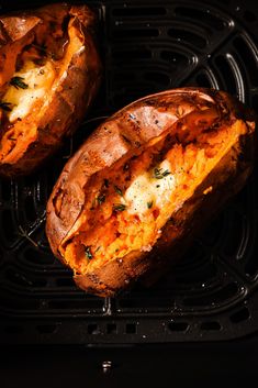 two baked sweet potatoes sitting on top of a black grill grate with herbs sprinkled on them