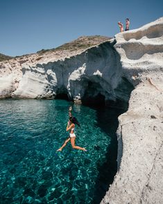 a woman jumping into the water from a cliff