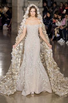 a model walks down the runway in an off - white gown with flowers on it