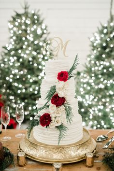 a white wedding cake with red flowers and greenery sits on a gold platter