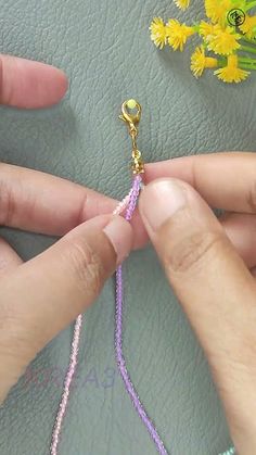 two hands are working on a beaded bracelet with beads and flowers in the background