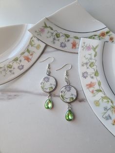 Broken China multicolor floral spring plate dangle earrings Cut and ground to 16mm circles and set in a 16mm stainless steel setting. Finished with a green gem charm. What is pictured is what you receive.  All items are pre-made, complete prior to posting, and one of a kind.  All New Plate, Who Dish? jewelry is made from used dishes or silverware so there may be imperfections but this is part of what makes each piece one of a kind! While New Plate, Who Dish? jewelry is made from plates and silve Broken Pottery Jewelry, Plates And Silverware, Pottery Jewelry, Green Gem, Spring Earrings, Broken China, China Plates, Green Gems, Oct 31