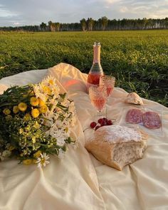 a bottle of wine, bread and flowers on a blanket in the middle of a field