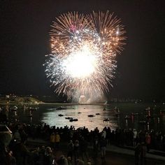 fireworks are lit up in the night sky over a body of water with boats on it