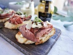 a wooden cutting board topped with slices of bread covered in meat and cheese on top of it