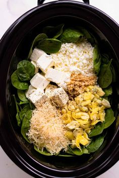 spinach, cheese and other ingredients in a crock pot on a white table