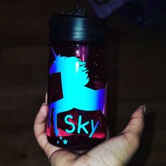 a hand holding a glass jar with the word sky painted on it in blue and pink