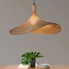 a large bamboo light hanging over a wooden table with a plant in the middle and plates on the side