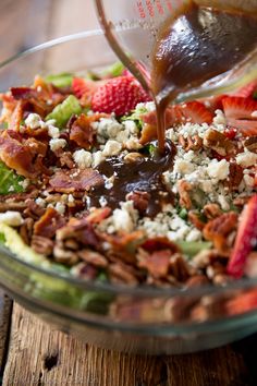 someone pouring dressing into a salad with strawberries and pecans