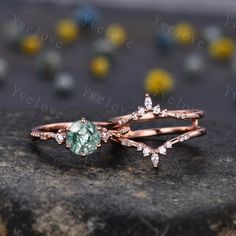 two rose gold wedding rings with green and white diamond accents on top of a rock