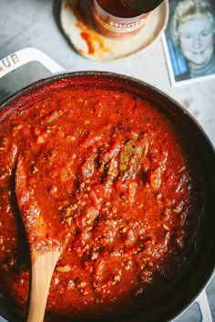 a wooden spoon in a saucepan filled with red sauce and meatballs on the side