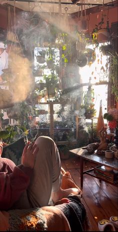 a woman sitting on top of a couch in a living room filled with potted plants