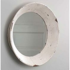 a round mirror hanging on the wall next to a white painted wooden door with peeling paint