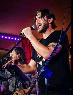 a man singing into a microphone while standing in front of another man with a guitar