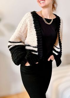 a woman standing in front of a white wall wearing a black and white cardigan