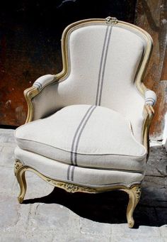 an old chair with white and gold trimmings sitting on the ground in front of a building