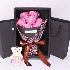 a teddy bear sitting next to a bouquet of pink roses in a black gift box