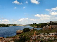 a body of water surrounded by rocks and greenery under a blue sky with clouds