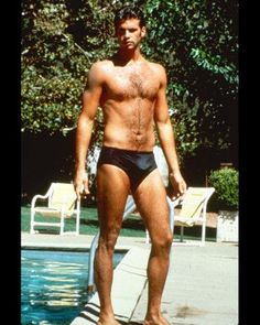 a man standing in front of a swimming pool wearing a black swim suit and no shirt