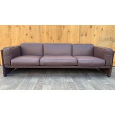 a purple leather couch sitting on top of a wooden floor next to a wood wall