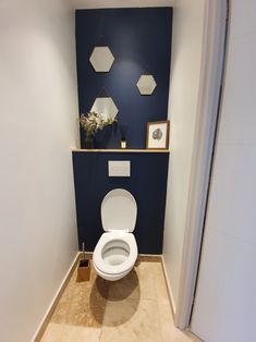 a white toilet sitting inside of a bathroom next to a blue wall with hexagonal mirrors on it