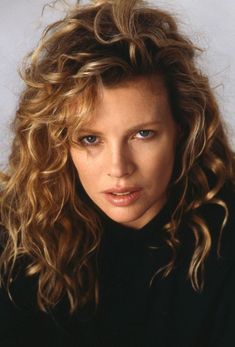 a close up of a person wearing a black shirt and long curly hair with blue eyes