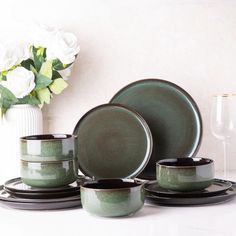 a set of green dishes and cups on a white table with flowers in the background