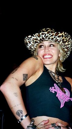 a woman wearing a leopard print hat and black tank top with tattoos on her arms