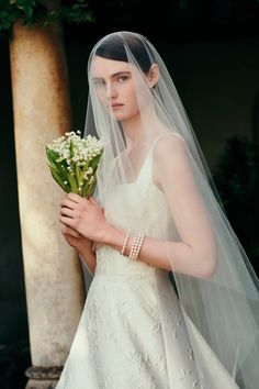 a woman in a white wedding dress holding a bouquet of flowers and wearing a veil