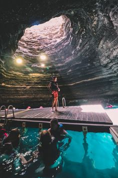 some people are swimming in the water and one is standing on a dock while others watch