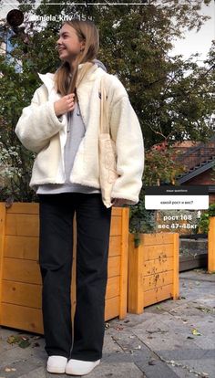 a woman standing next to a wooden planter with her hands in her pockets and looking off into the distance