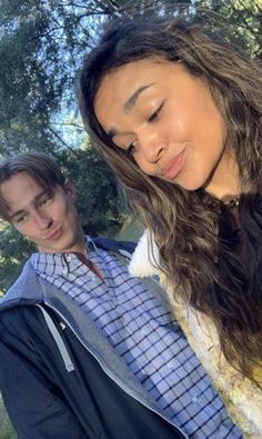 a man and woman standing next to each other in front of trees with their eyes closed