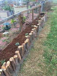 a fenced in garden area with wood logs and plants growing out of the ground