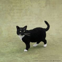 a black and white cat figurine standing on a green cloth covered surface, looking at the camera