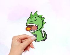 a hand holding up a sticker with a green dragon on it's face