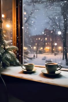 two cups sit on a window sill in front of a snowy scene with christmas lights