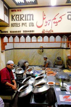 some people are preparing food inside of a restaurant with arabic writing on the sign above them