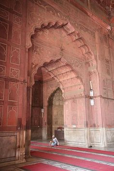 a person sitting on the floor in an ornate building with red carpet and arches,