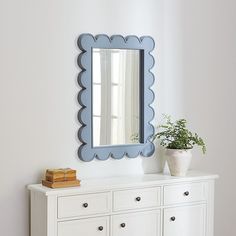 a white dresser with a blue mirror on top of it and a potted plant