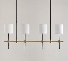 four lamps are hanging from a brass bar with white shades on them and one light is turned off