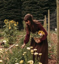 a woman in a brown dress is picking sunflowers from a garden with yellow flowers