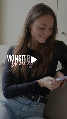 a woman sitting on a couch looking at her cell phone and smiling with the text monster wars in front of her