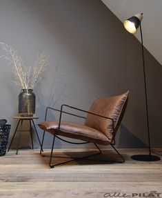 a brown chair sitting next to a lamp on top of a wooden floor