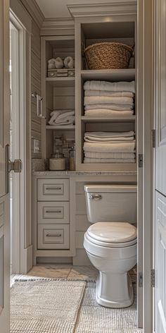 a white toilet sitting inside of a bathroom next to a closet filled with folded towels