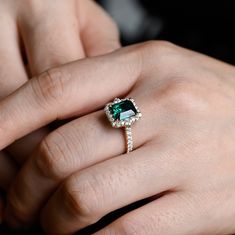 a close up of a person's hand wearing a ring with an emerald and diamond center