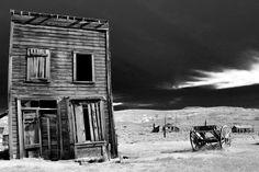 black and white photograph of an old wooden building in the middle of nowhere with storm clouds overhead