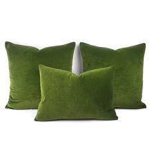 three green velvet pillows sitting on top of a white surface with one pillow in the middle