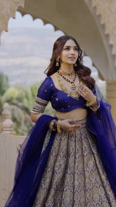 a woman in a blue and gold lehenga is posing for the camera with her hands on her hips