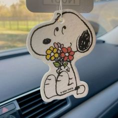 a snoopy car air freshener hanging from the dash board with flowers in it