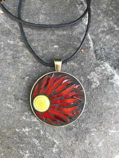 a red and yellow pendant on a black leather cord with a white circle in the center